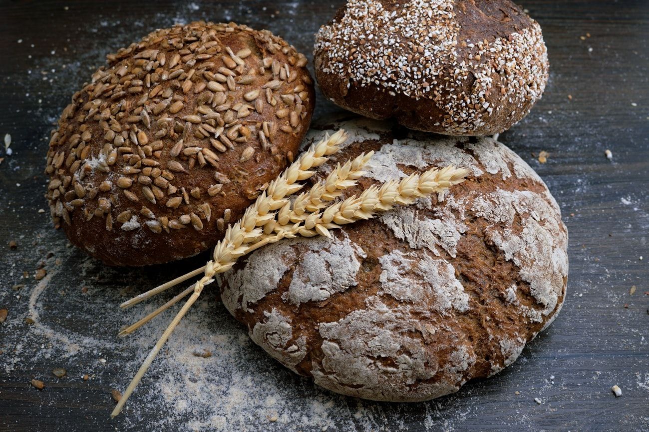 Rustic loaves of seeded and floured bread on a dark surface.